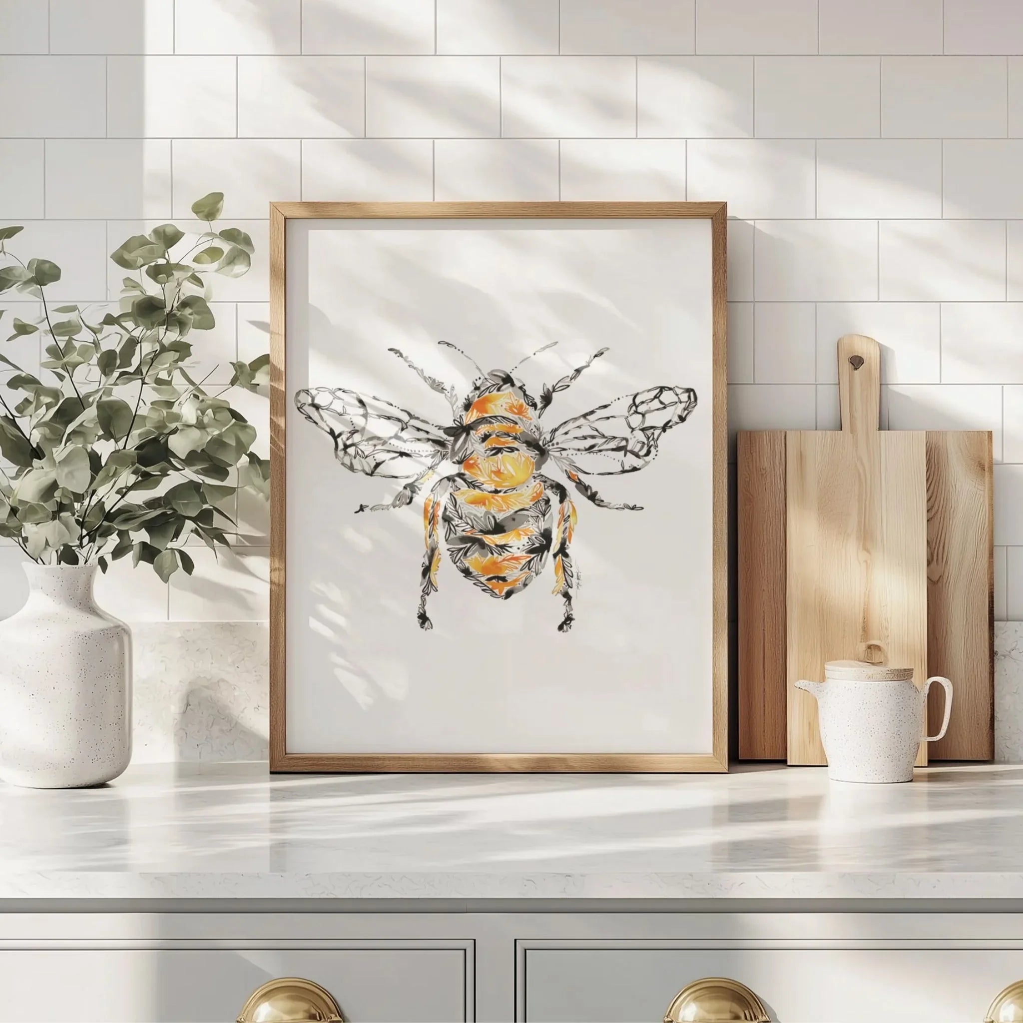Framed honey bee art print with floral details, displayed on kitchen counter beside greenery and cutting boards