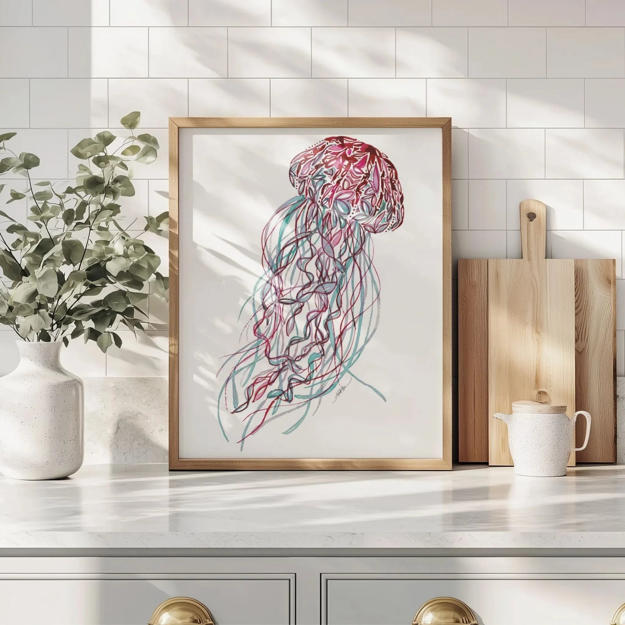 Framed jellyfish wall art print with colorful tentacles, displayed on kitchen counter beside plants and cutting boards
