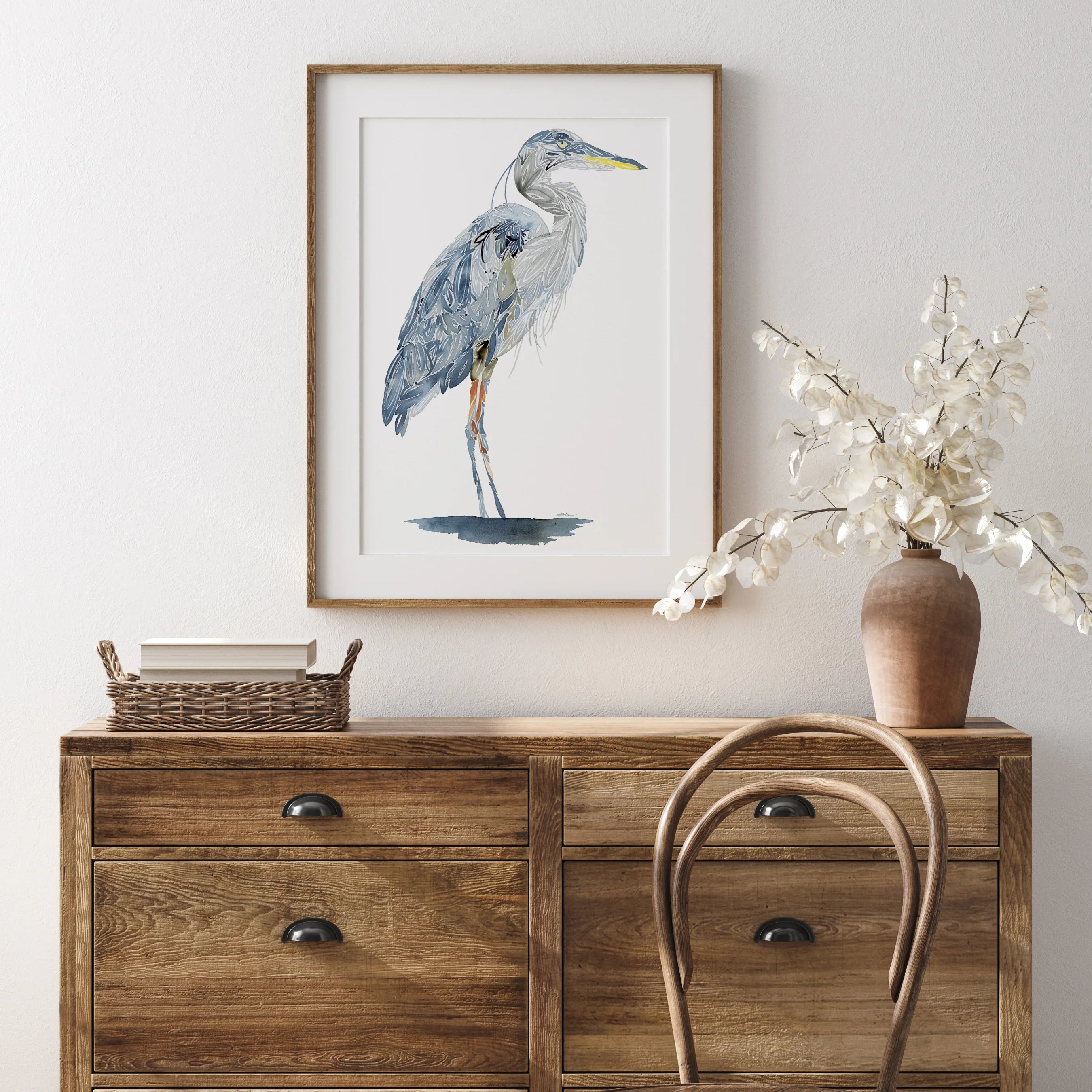 Framed heron wall art above wooden dresser with vase and chair, perfect for home decor