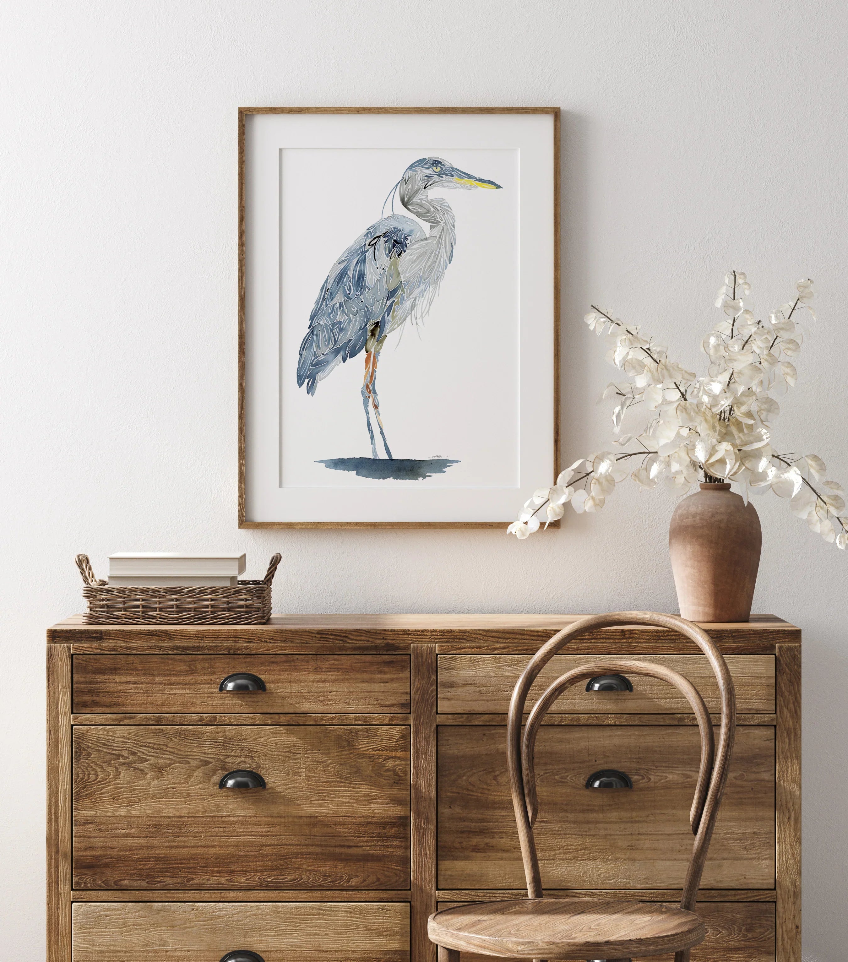 Framed heron wall art above wooden dresser with vase and chair, perfect for home decor